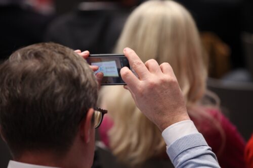 Ein Teilnehmer macht mit seinem Smartphone ein Foto der Präsentation.